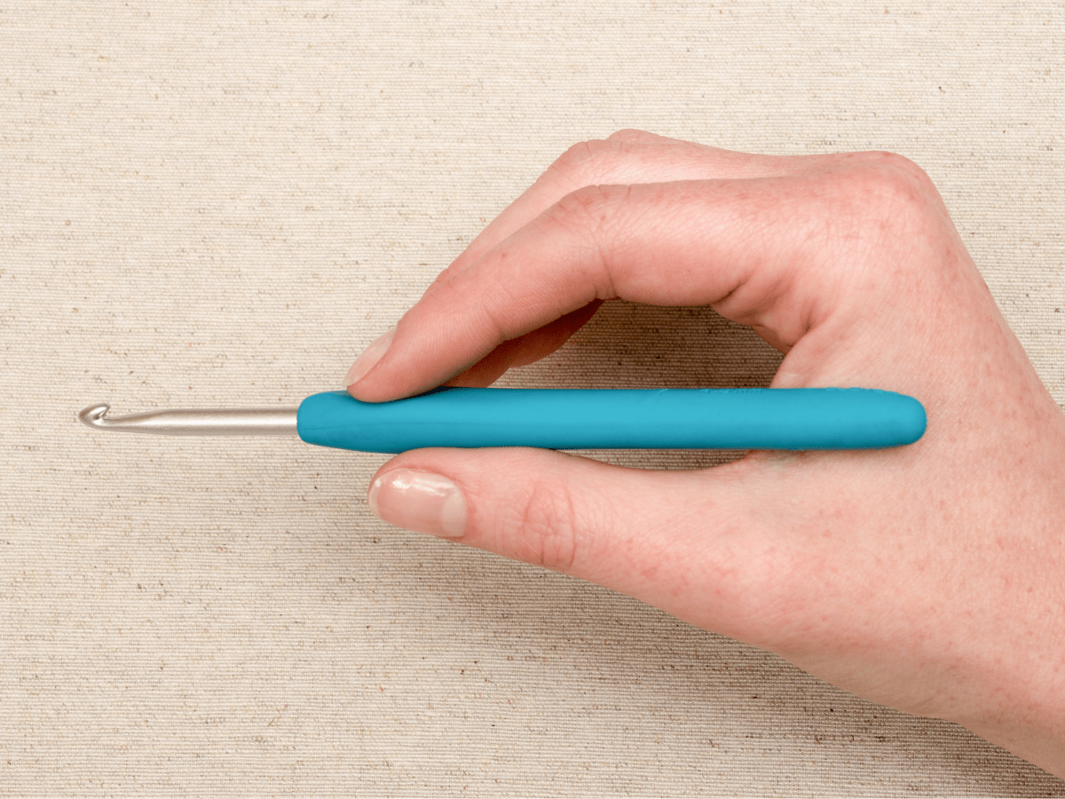 Hand holding a crochet hook in a pencil grip 