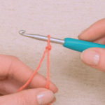 Hand holding a crochet hook with a slip knot in peach colour yarn