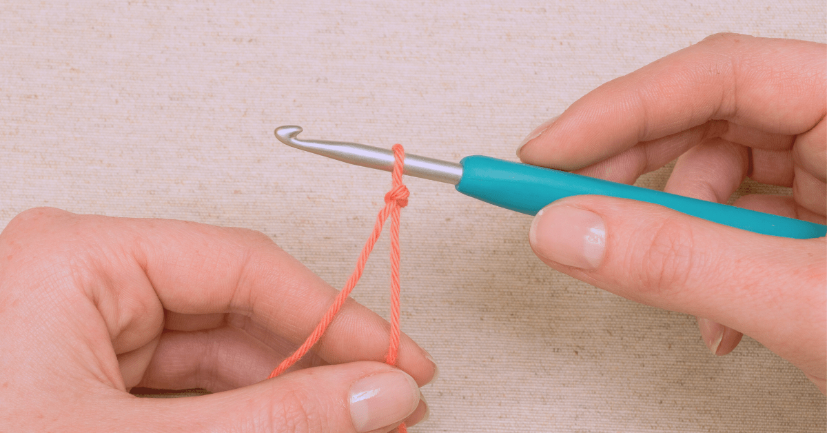 Hand holding a crochet hook with a slip knot in peach colour yarn